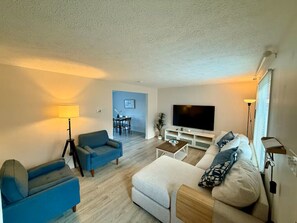 Een woonkamer met een bank, fauteuil, televisie en lamp.