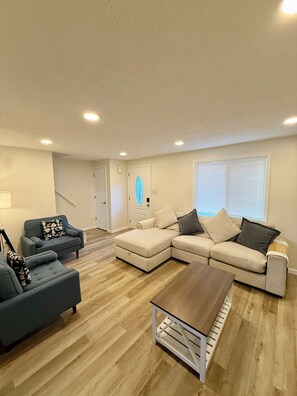 A living room with a sectional sofa, a small sofa, a coffee table, and a staircase leading to another room. - Modern 3BR Townhouse Close To Downtown Pittsburgh (Pittsburgh)