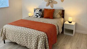 Un dormitorio con una cama, dos mesitas de noche, una pared decorada con tres flores y una ventana con persianas.