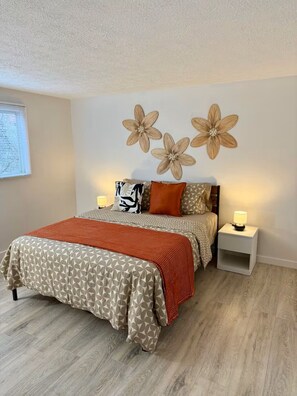 Un dormitorio con una cama, dos mesitas de noche, una pared decorada con tres flores y una ventana con persianas.