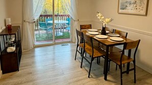 Un comedor con una mesa dispuesta para cuatro personas, una puerta corrediza de vidrio que da a un patio exterior y un cuadro en la pared.