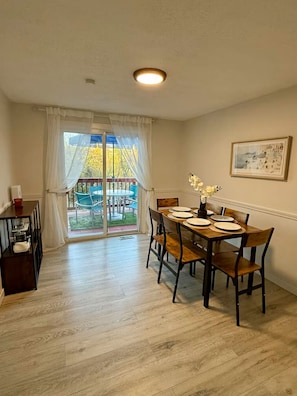 Un comedor con una mesa dispuesta para cuatro personas, una puerta corrediza de vidrio que da a un patio exterior y un cuadro en la pared.