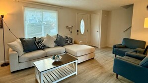 Una sala de estar con un sofá seccional, una mesa de centro, un sillón azul y una puerta con un ventanal esmerilado.