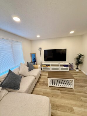 A modern living room with a beige sofa, a coffee table, a flat-screen TV, and a potted plant. - Modern 3BR Townhouse Close To Downtown Pittsburgh (Pittsburgh)