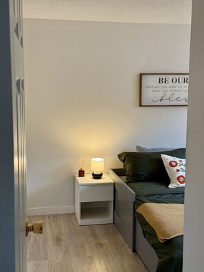 A bedroom with a bedside table, a lamp, a bed with a pillow, and a framed quote on the wall. - Modern 3BR Townhouse Close To Downtown Pittsburgh (Pittsburgh)