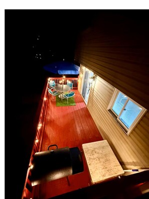 Una terraza con una parrilla, mobiliario exterior y una ventana con persianas.