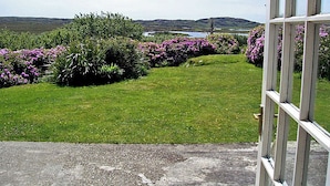 A view of a garden with various plants and a distant body of water. - 2 Bed in Ballyconneely (oc-i231) (Leitirshask)
