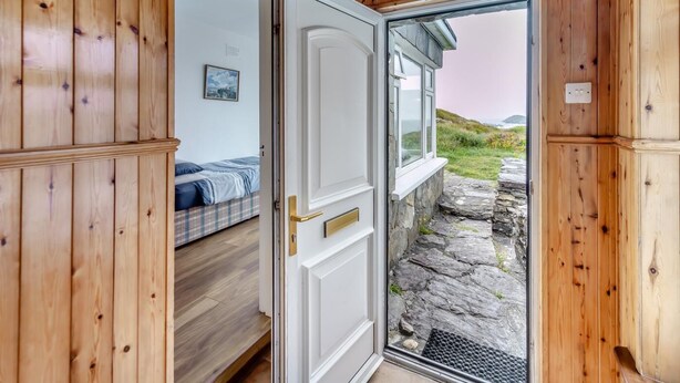 Un interior de madera con una cama, una puerta que da al exterior y un sendero de piedra.