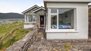 Una casa de piedra con un ventanal grande, una puerta y vistas al mar.