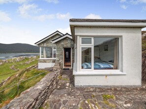 Ein Steinhäuschen mit großem Fenster, einer Tür und Blick auf das Meer.