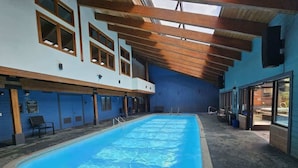 Een binnenzwembad met een helderblauw wateroppervlak, houten balken in het plafond en een blauwe muur.