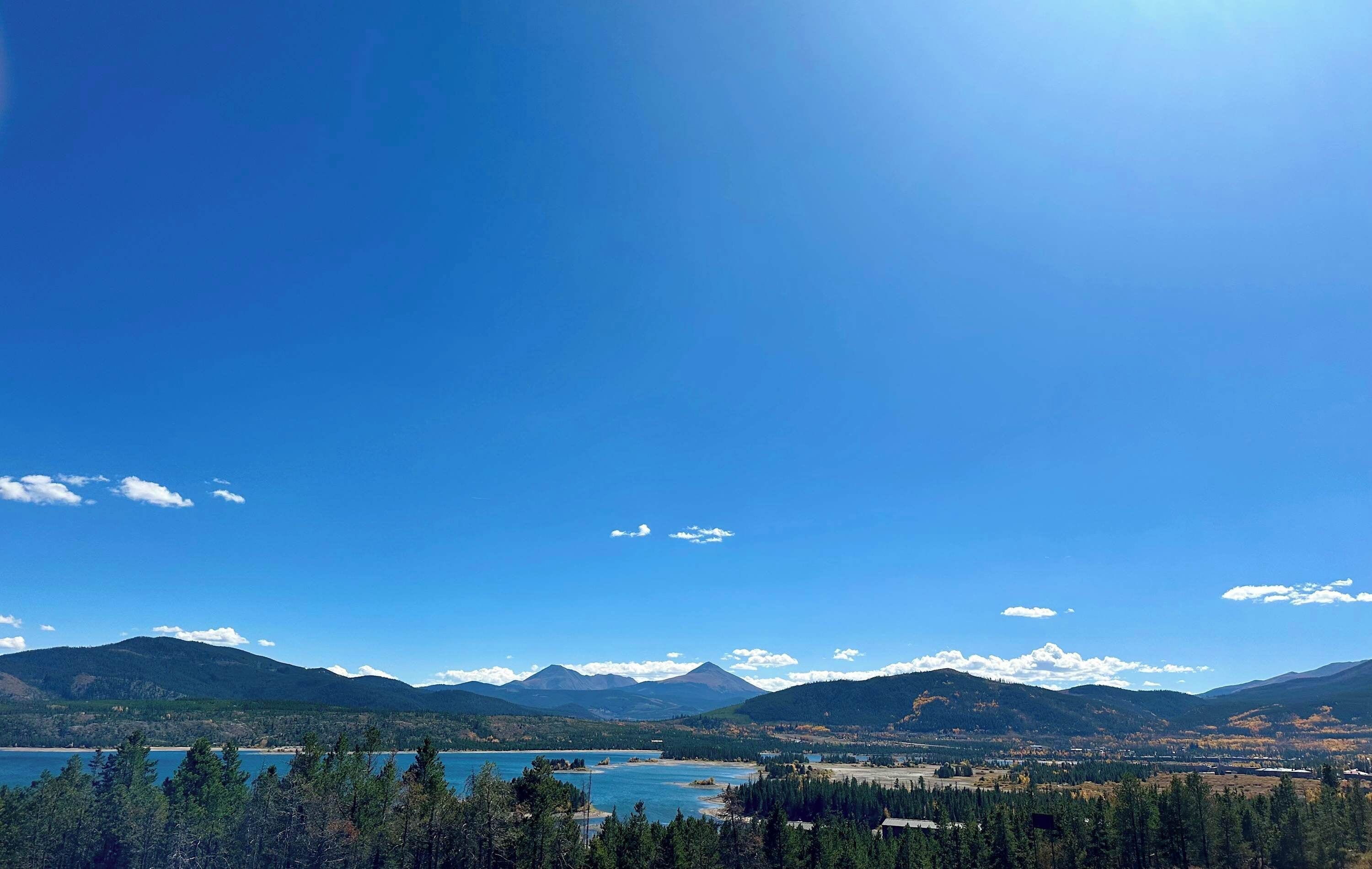 A mountainous landscape with a clear sky, a lake, and forested areas.