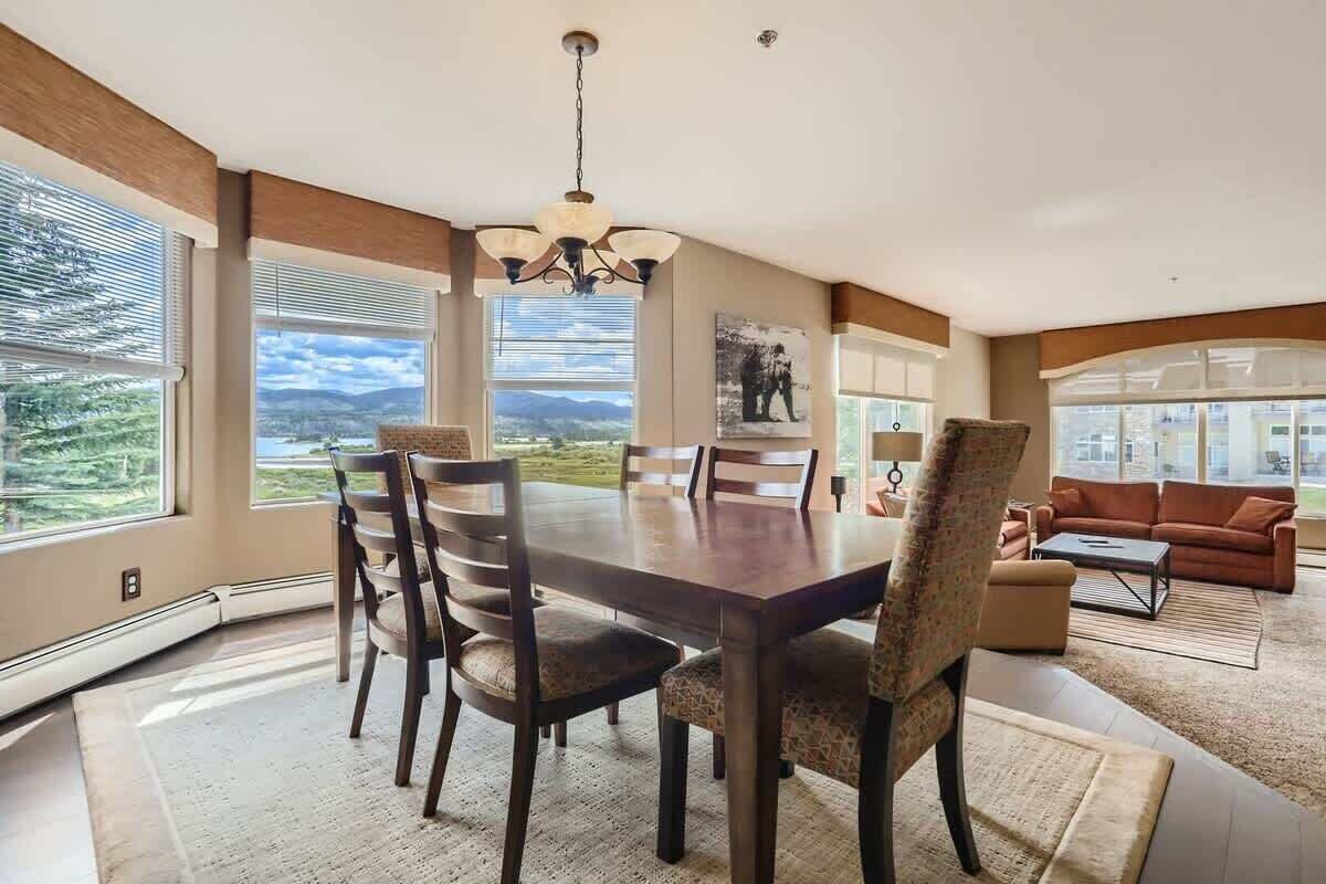 A spacious dining area with a large table and chairs, a chandelier, and large windows offering a view of the outdoors.