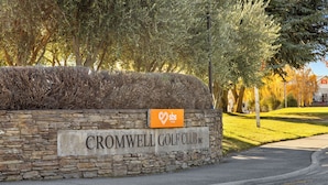 A stone wall with a sign for Cromwell Golf Club Inc. and a bank logo. - Get Away By The Green - Cromwell Holiday Home (Cromwell)