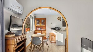 A modern kitchen with wooden cabinets, a dining area with a table and chairs, a TV on a wooden stand, and a large arched doorway leading to another room. - Get Away By The Green - Cromwell Holiday Home (Cromwell)