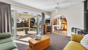 A modern living room with a sofa, a coffee table, and a TV. There is a sliding glass door leading to an outdoor area. - Get Away By The Green - Cromwell Holiday Home (Cromwell)