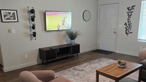 Ett vardagsrum med en tv, en soffa, ett soffbord och en dörr.