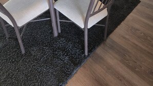 Ett modernt kök med vita skåp, ett matbord i glas med fyra stolar och en svart matta.