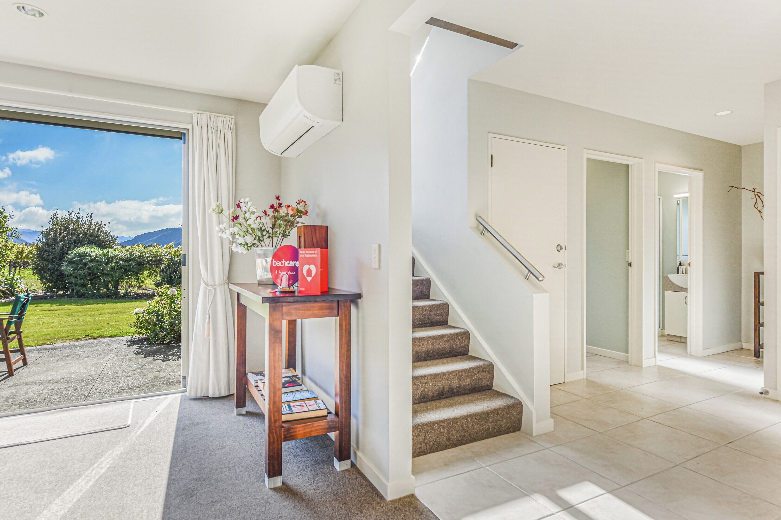 A modern interior with a staircase, a table with a vase, and a view of a garden.