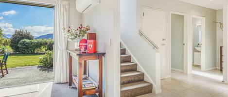 A modern interior with a staircase, a table with a vase, and a view of a garden.