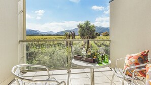 A balcony with a table, chairs, and a bottle of wine. - Vineyard View - Blenheim Holiday Home (Blenheim)