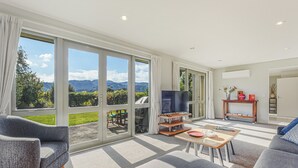 A spacious living room with large windows, a flat-screen TV, and a cozy seating area. - Vineyard View - Blenheim Holiday Home (Blenheim)