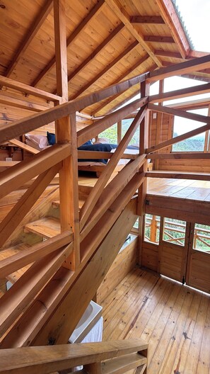 Interior de madera con una escalera, una cama y vistas al exterior.