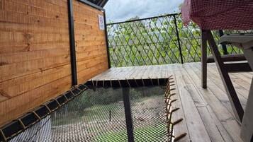 Un espace extérieur abrité, doté d’une terrasse en bois, d’un trampoline à mailles métalliques et d’une nappe à carreaux.