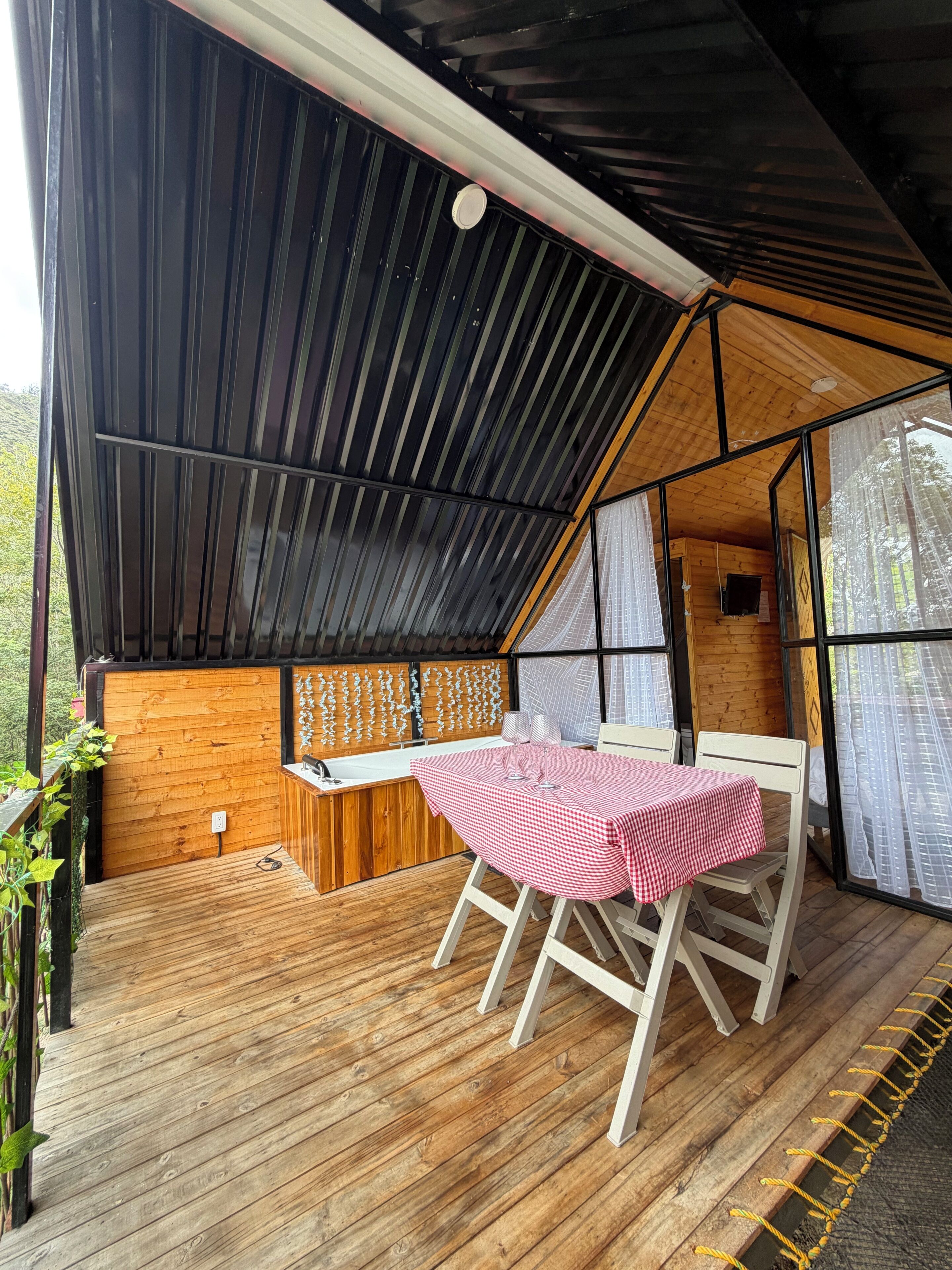 A wooden deck with a table and chairs, a wooden bench, and a window with curtains.