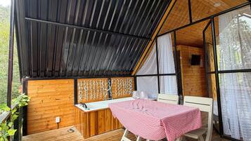 A wooden deck with a table and chairs, a wooden bench, and a window with curtains.