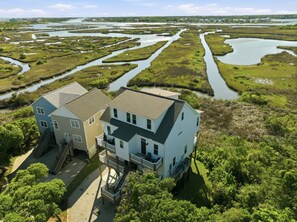 Ein zweistöckiges Haus mit einer Veranda, umgeben von einer sumpfigen Landschaft mit Wasserläufen.