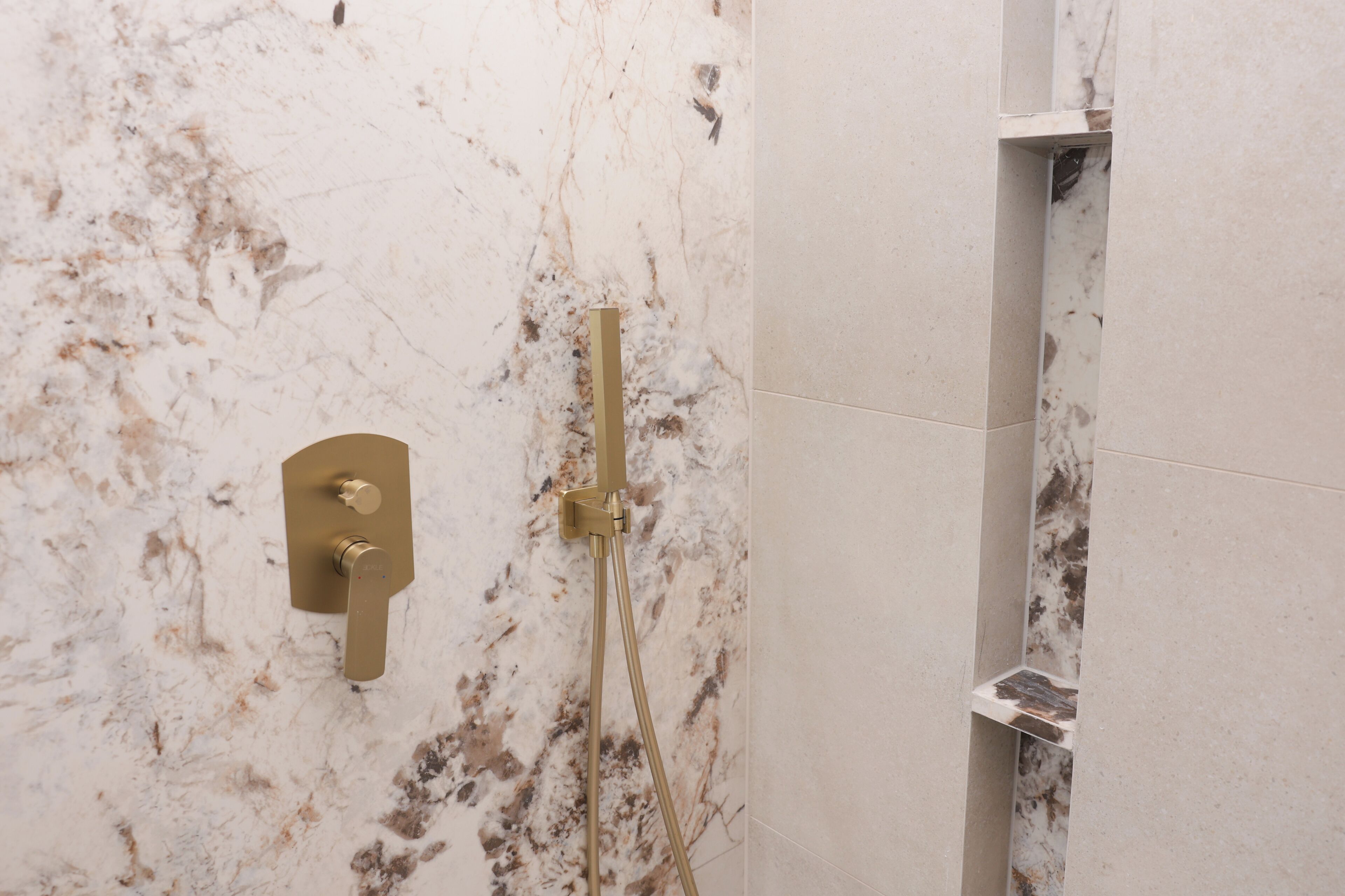 A bathroom with a marble wall, a gold showerhead, and a wall-mounted control panel.