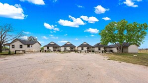 A row of single-story buildings with a gravel driveway and a large tree to the right. - Vista Moon Main House - Pool, Chapel, Fire Pit (Fredericksburg)