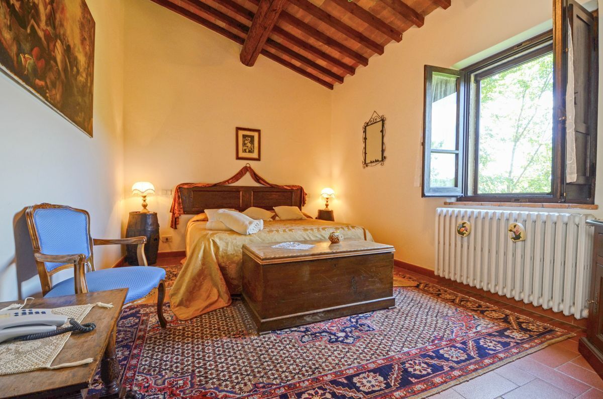 A bedroom with a bed, a chest of drawers, a chair, a table, a radiator, and a window.