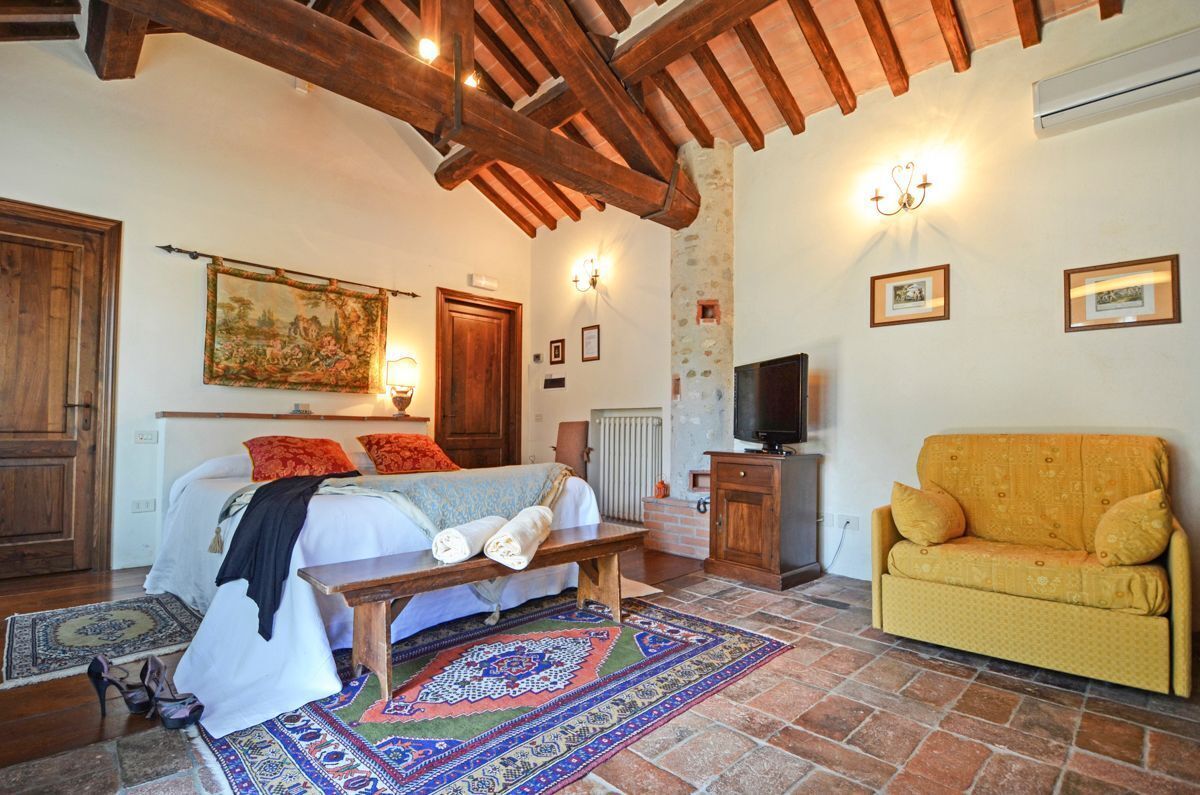 A room with a bed, a sofa, a bench, a television, and a stone wall.