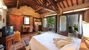 A rustic bedroom with a large bed, wooden furniture, and a stone wall. - Villa Il Gufo - Seven Bedroom Villa, Sleeps 20 (Anghiari)