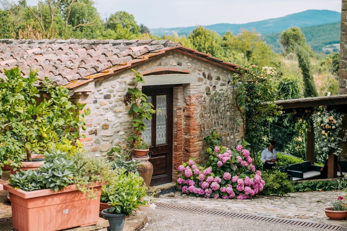 A stone building with a tiled roof, surrounded by potted plants and flowers.