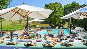 An outdoor dining area with tables set for a meal, surrounded by umbrellas, a pool, and lounge chairs. - Villa Il Gufo - Seven Bedroom Villa, Sleeps 20 (Anghiari)