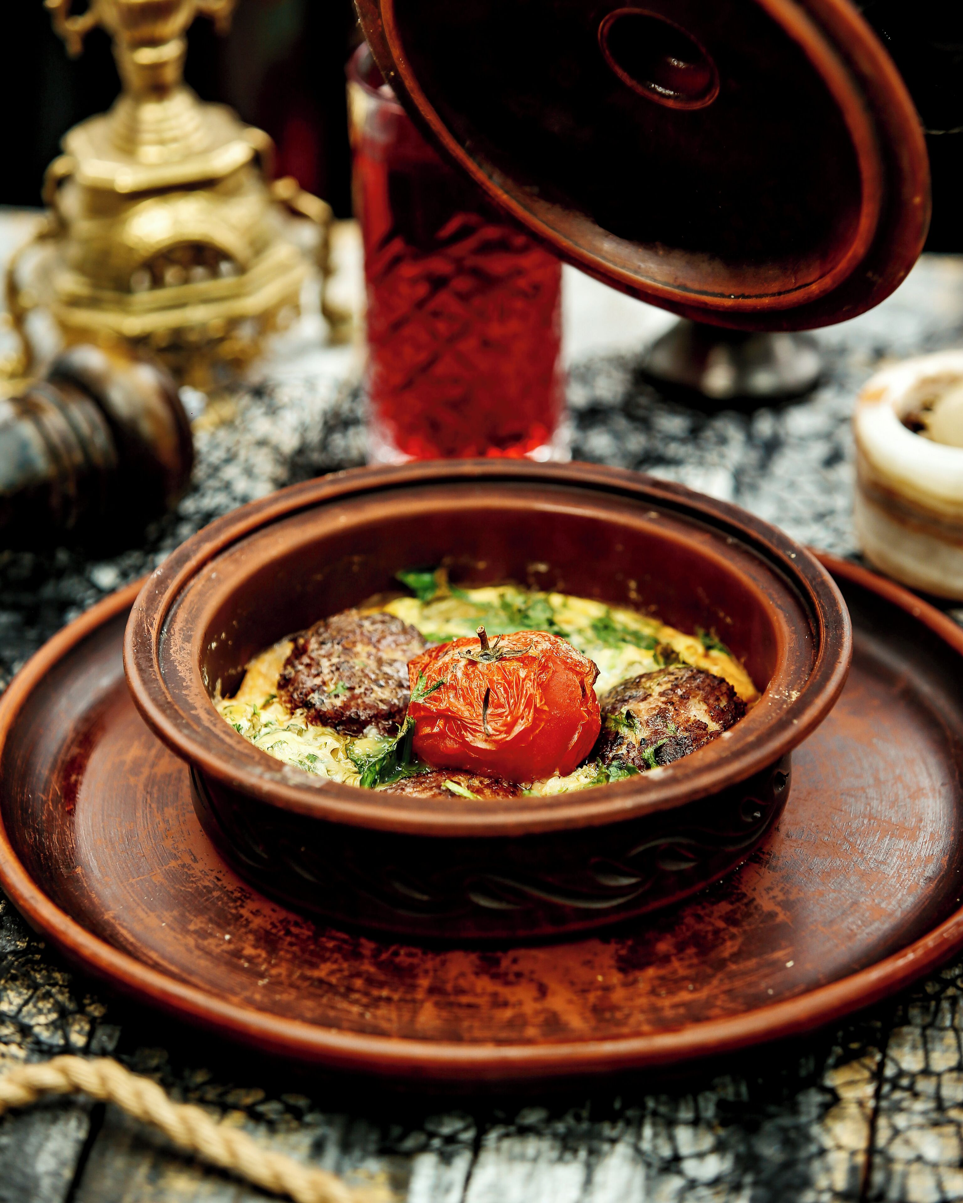 Un plato de arcilla tradicional con tapa, un recipiente rojo para especias y un dispensador de aceite de latón sobre una superficie texturizada.