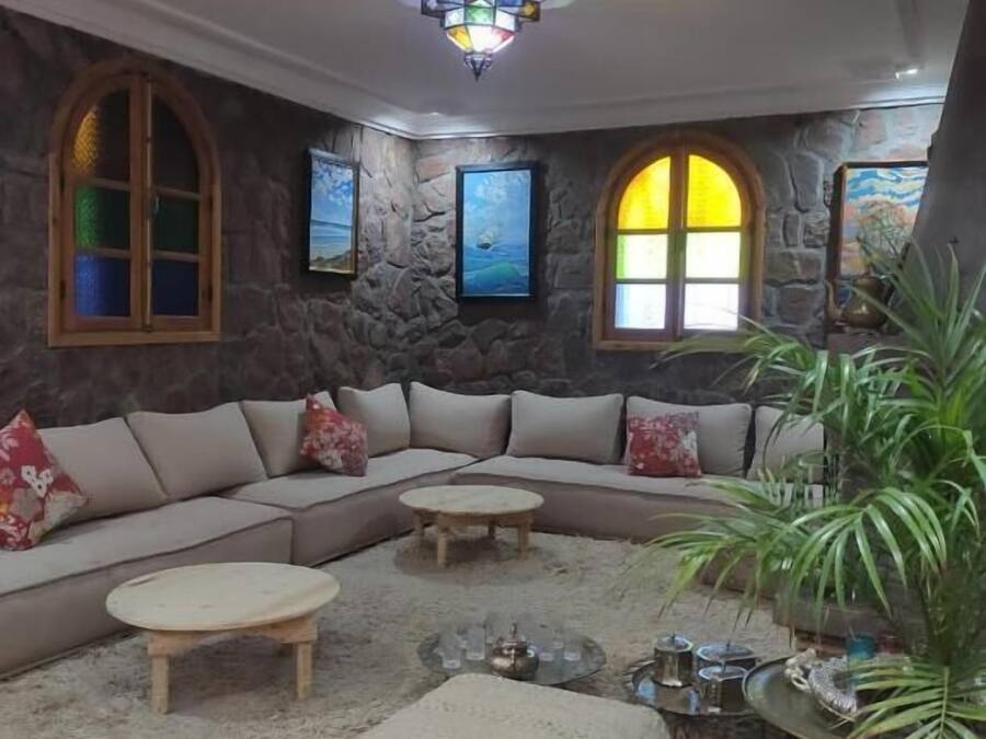 Uma sala de estar acolhedora com parede de pedra, sofá de canto, mesa de centro e uma janela grande com vista.