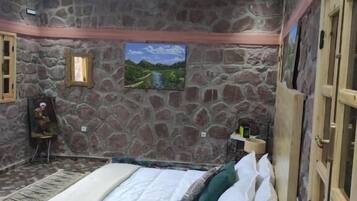 Un dormitorio con pared de piedra, una cama con ropa blanca, un cabecero de madera y una pequeña mesita de noche de madera.