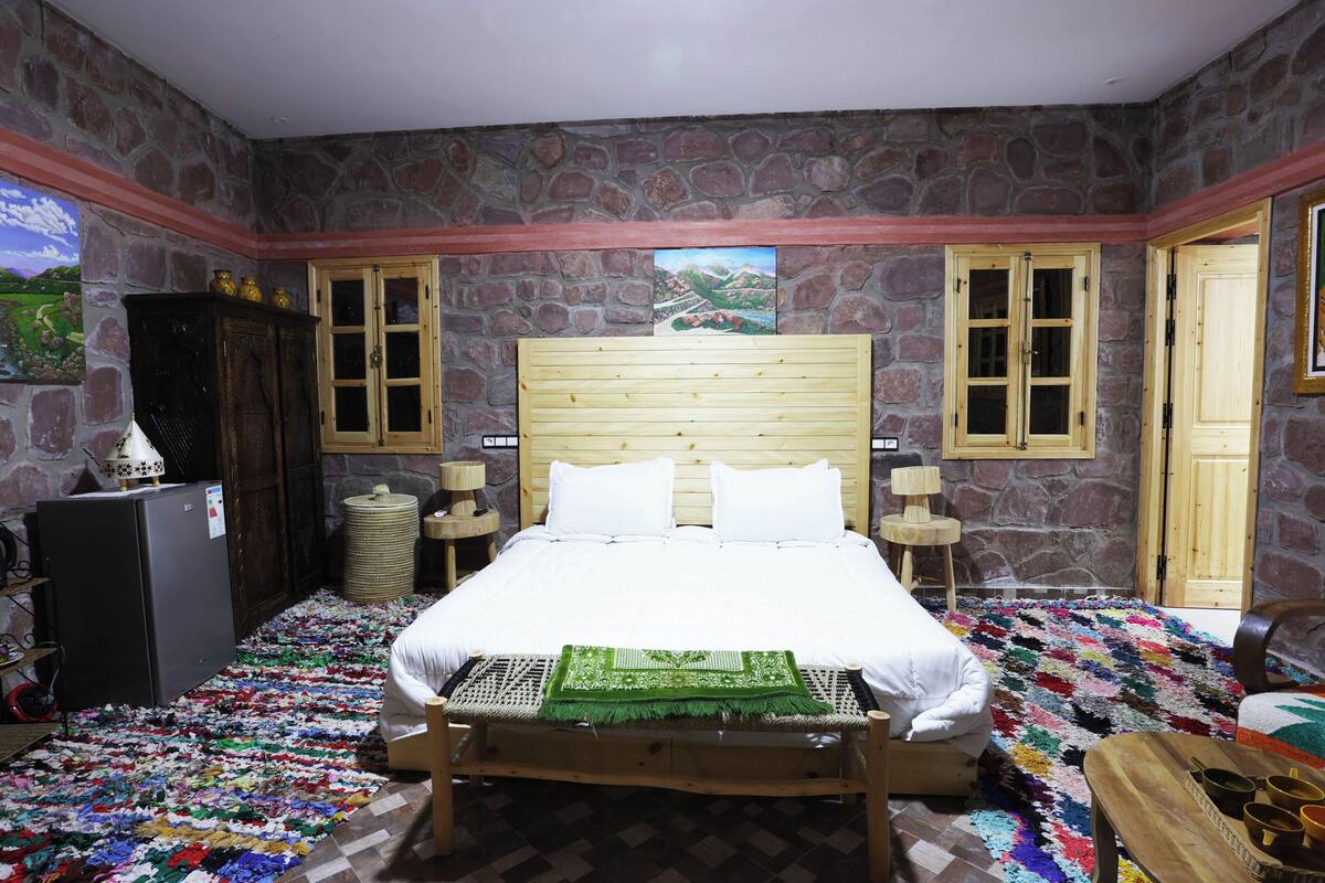 Un dormitorio con pared de piedra, cama de madera, una mesita y un armario.