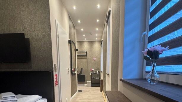 A hotel room with a bed, a small table, a window with blinds, a mirror, and a door leading to a bathroom. - Suite-Pauli (Hamburg)