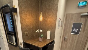 A small, modern room with a wooden table, two black chairs, a potted orchid, a light fixture, a door, and a wall-mounted control panel. - Suite-Pauli (Hamburg)