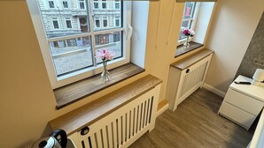 A kitchenette with a window, a radiator, a white cabinet, and a small table with a kettle and a vase of flowers. - Suite-Pauli (Hamburg)
