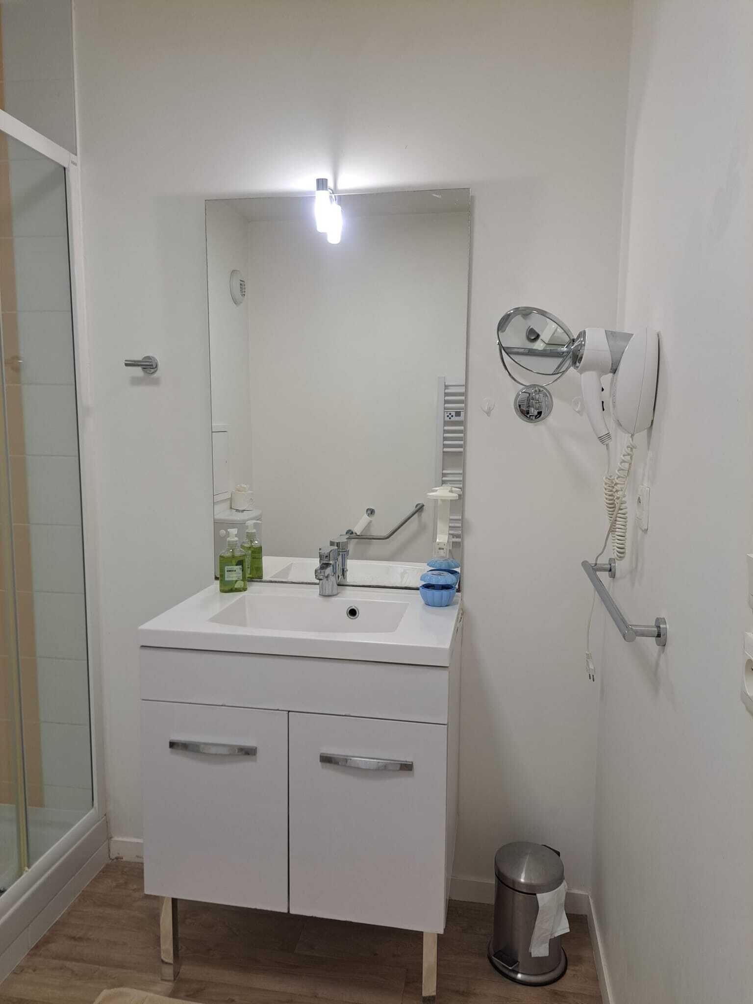 Une salle de bain avec un lavabo blanc, un miroir et un sèche-cheveux fixé au mur.