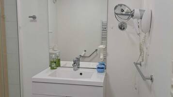 Une salle de bain avec un lavabo blanc, un miroir et un sèche-cheveux fixé au mur.