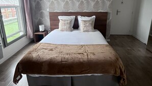 A bedroom with a large bed, a nightstand, a lamp, a window with curtains, and a patterned wall. - Cosy studio • 5 min from station and center - Very bright and quiet (Amiens)
