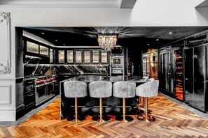 Une cuisine moderne dotée d’un îlot central, de tabourets de bar, d’un lustre et d’un réfrigérateur à vin.