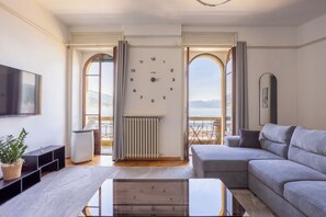 A living room with a sofa, a TV, a clock, and a view of the outdoors. - Prestige with lake view in the historic heart of Stresa (Stresa)